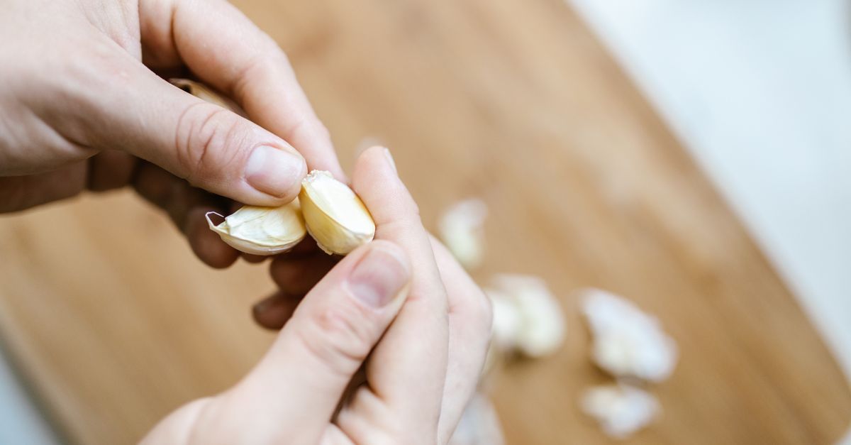Mãos descascando dentes de alho sobre uma tábua de madeira