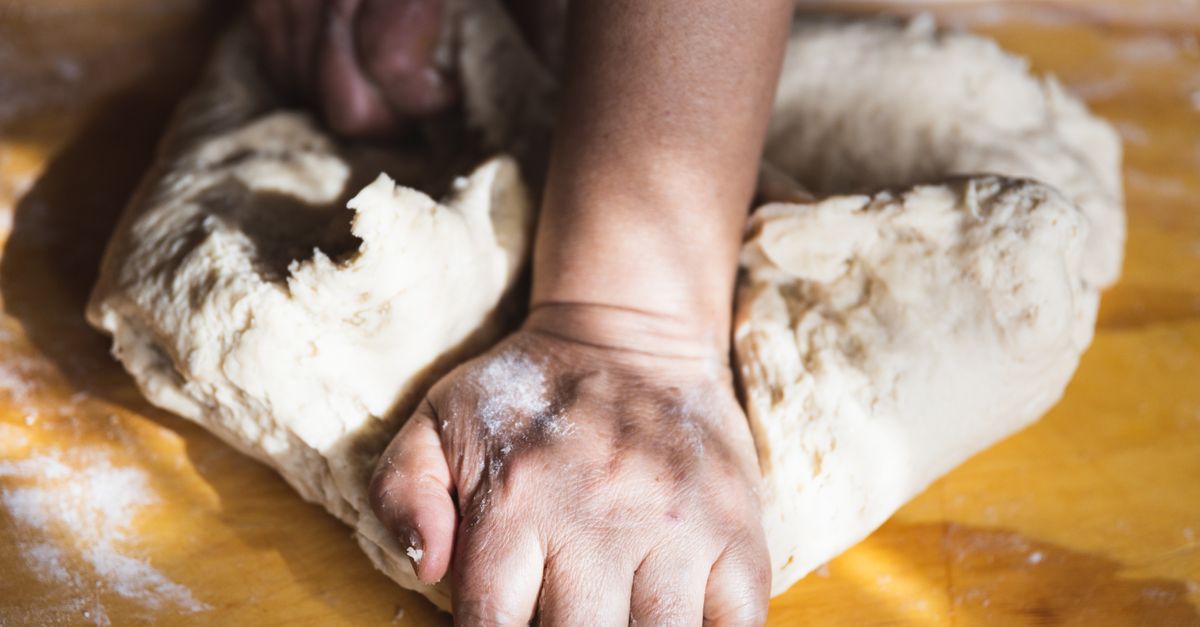 Mãos sovando massa de pão sobre uma bancada de madeira