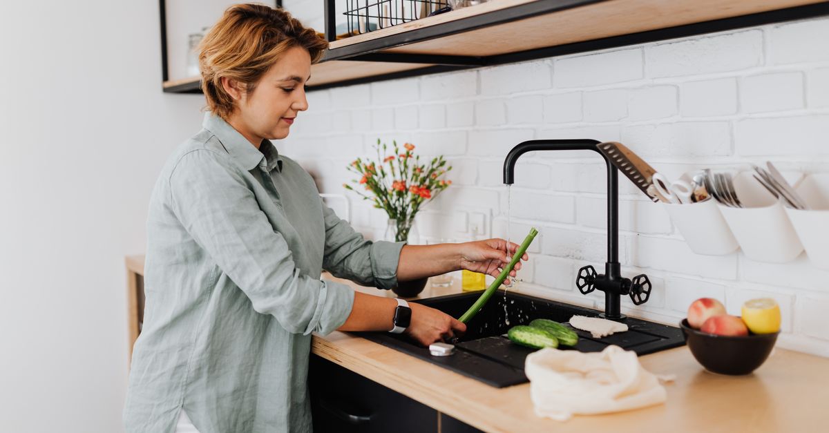 Pessoa lavando legumes na pia de uma cozinha clara
