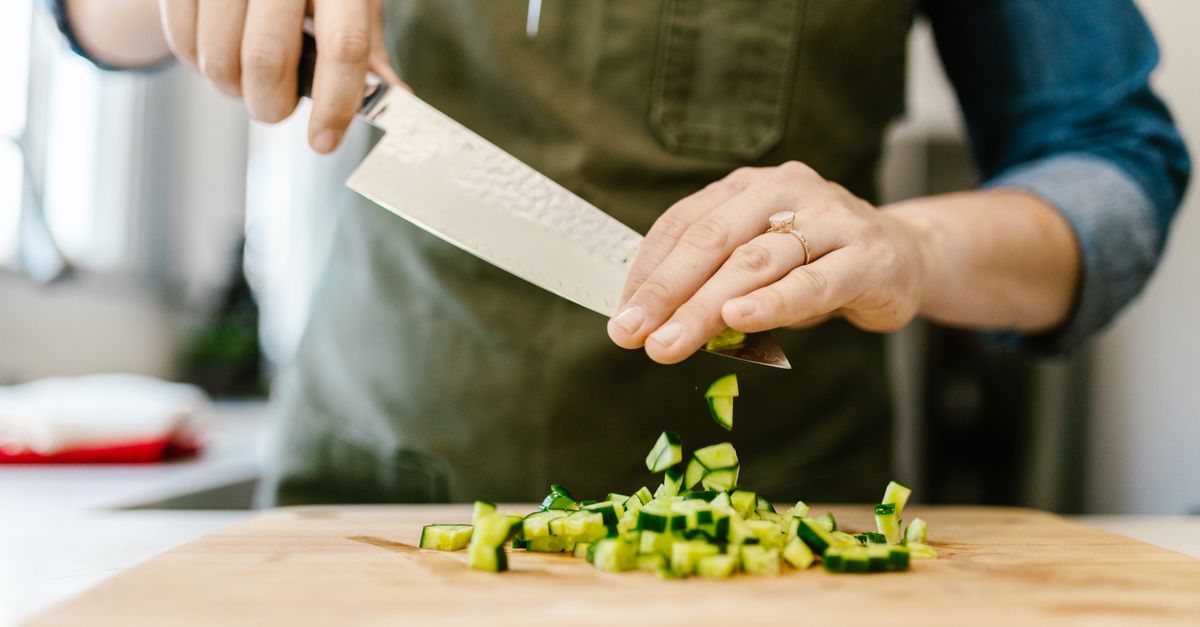 Faca de cozinha cortando pepino em cubos pequenos sobre a tábua