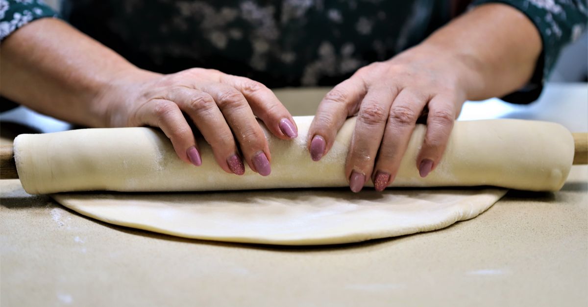 Mãos enrolando uma massa de torta sobre a bancada